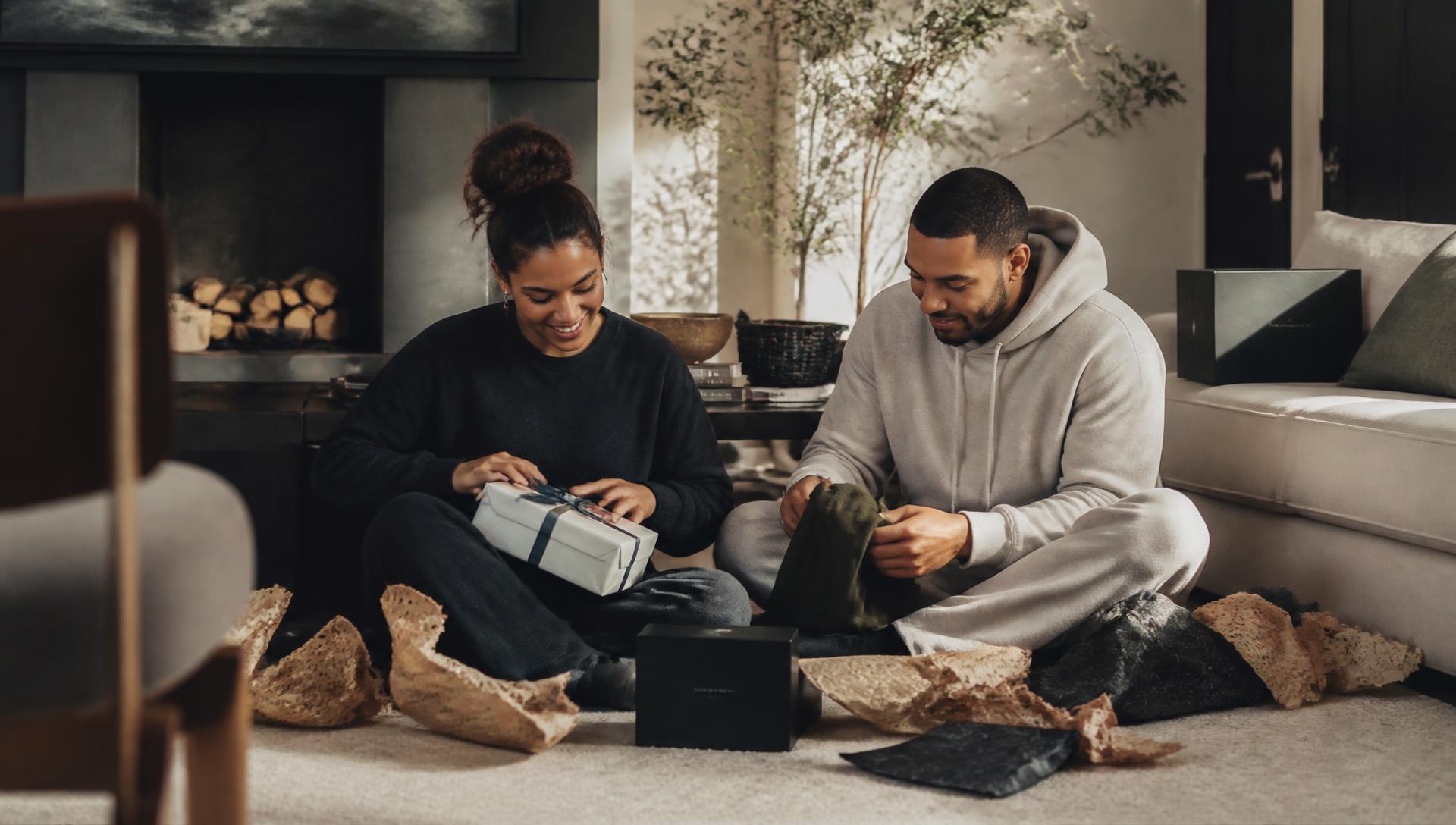 A couple sitting on the floor of their living room opening gifts together