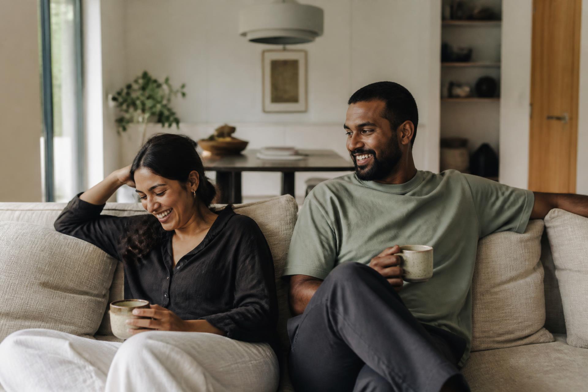 A relaxed modern couple with coffee on a linen sofa in their bright, lived-in home